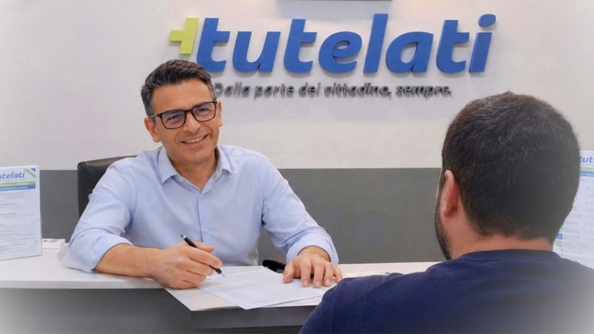 Consulenza al bancone di Più Tutelati Trani: un consulente spiega una bolletta a un cliente, con il logo Tutelati a parete